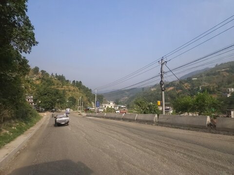 Scenic mountain highway passing through hilly terrain with vehicles traveling along a dusty road construction section.