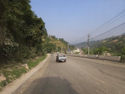 Scenic mountain highway passing through hilly terrain with vehicles traveling along a dusty road construction section.