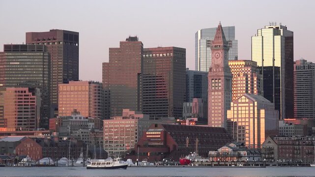 Panoramic view of Boston skyline with Customs House tower and harbor at sunset.