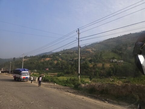 Scenic mountain highway passing through hilly terrain with vehicles traveling along a dusty road construction section.