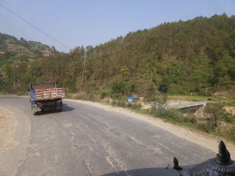 Scenic mountain highway passing through hilly terrain with vehicles traveling along a dusty road construction section.