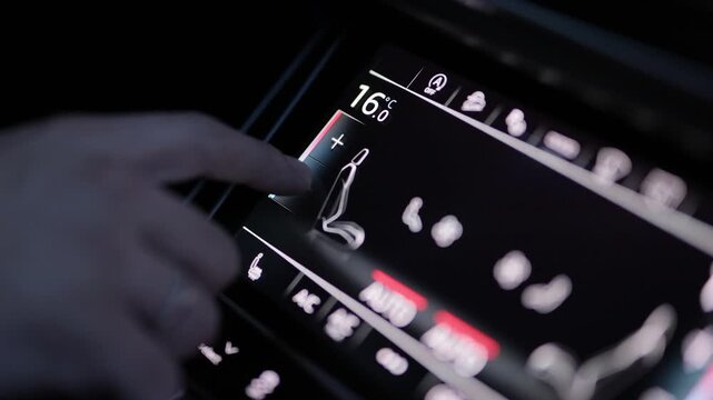 A hand adjusts the climate control system in a car. Male hand regulating the air conditioning control in a car. The warm glow of the controls shows the set temperature