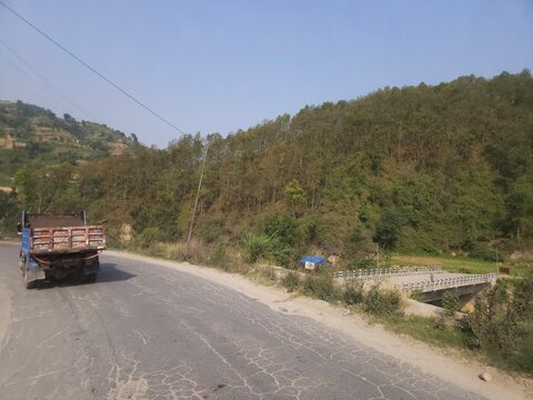 Scenic mountain highway passing through hilly terrain with vehicles traveling along a dusty road construction section.