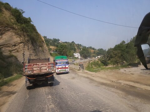 Scenic mountain highway passing through hilly terrain with vehicles traveling along a dusty road construction section.