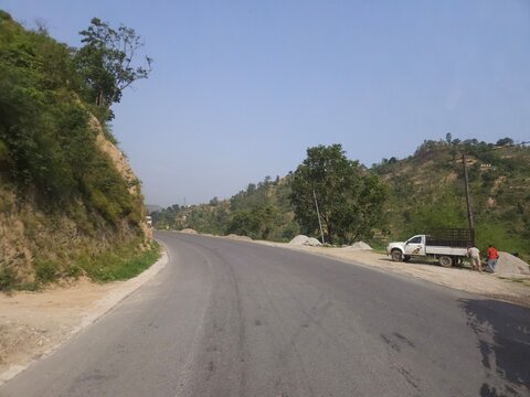 Scenic mountain highway passing through hilly terrain with vehicles traveling along a dusty road construction section. The footage showcases transportation infrastructure, regional connectivity.