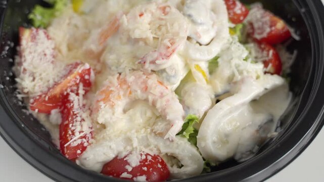 Delicious caesar salad with shrimp and calamari sprinkled with parmesan cheese in a takeaway container