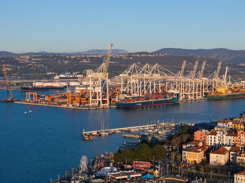 View of Kopers waterfront with boats in cargo port and city buildings along the shore under bright sky.