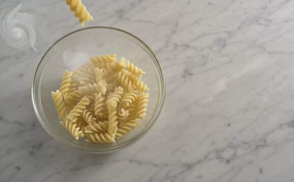 Steaming fusilli pasta dropping into a glass bowl
