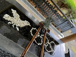 神社の手水舎にある龍の吐水口と八咫烏の形に並べられた小石 © LACCEC