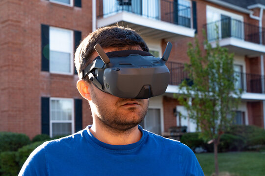 Horizontal shot of a man wearing FPV goggles and operating a drone controller, emphasizing immersive drone piloting, real-time first-person flight control, and cutting-edge aerial technology