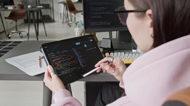 Over-shoulder shot of young Caucasian female programmer reviewing script iteration written by AI vibe coding assistant on tablet, circling components for improvement and crossing out mistakes