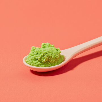 A spoon with bright green wasabi paste against a peach background
