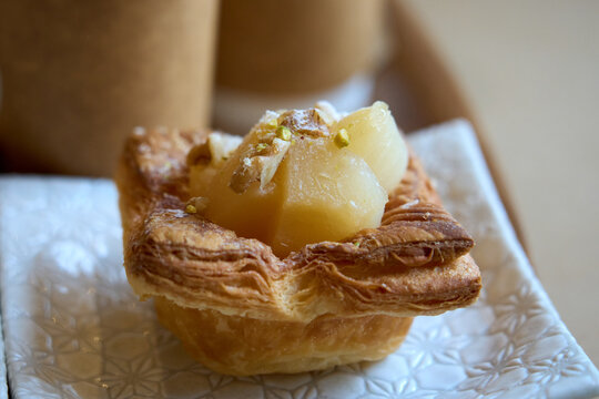 Pear danish pastry topped with chopped nuts and powdered sugar on a white plate.