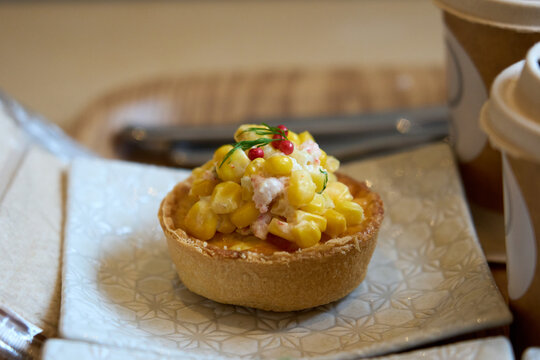 Close-up of a mini sweet corn quiche with colorful toppings in a cafe.