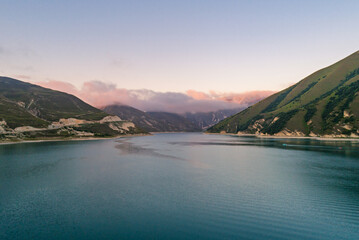 Naklejka premium Expansive Lake Kazenoy-Am nestled between steep green mountains under a pastel sky