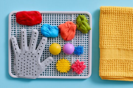 Hand therapy tools with colorful putty and textured balls on peg board with yellow towel