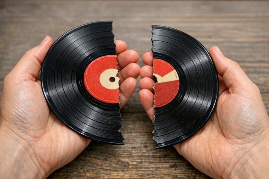 A person holding a broken vinyl record with a melancholic expression