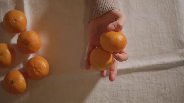 Hand arranging mandarins on linen table, food stylist sorting ripe citrus into pleasing layout, soft natural light, warm tones, textured peel and scattered fruit cluster, calm minimalist composition