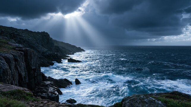 Dramatic coastal landscape with powerful sun rays breaking through storm clouds over a turbulent ocean and rugged dark cliffs.