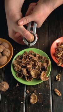 Hands cracking open walnut shells with a nutcracker, revealing the nut inside, surrounded by empty shells and whole walnuts on a wooden table