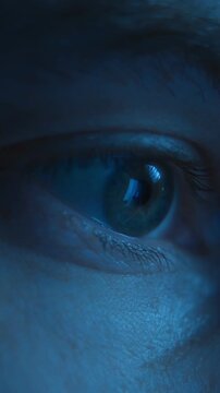 Close-up of man eyes looking with focus on a computer or smartphone display with the screen reflection in his pupil, working late at night or scrolling through a news feed. Vertical video