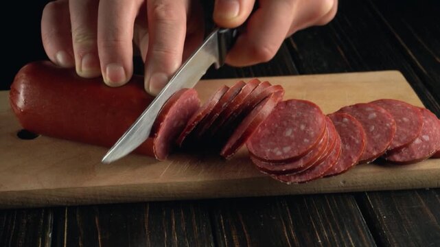 Hands slicing sausage into thin rounds on a wooden cutting board, showcasing the precision of the cutting technique in a well-lit kitchen setting
