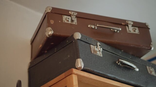 Stacked vintage suitcases on wooden shelf, collector organizing heirloom cases in warm attic light, worn leather, metal corners and aged patina evoke travel memories and cozy interior decor.
