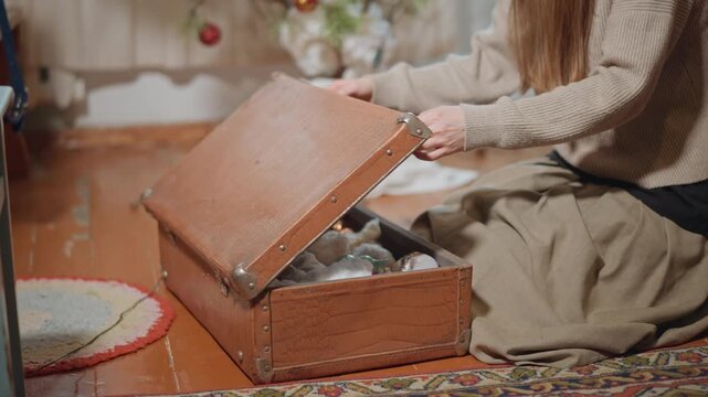 Caucasian woman opening vintage trunk filled with ornaments and cotton stuffing cozy living room, wool sweater, patterned rug, wooden floor gentle archivist moment as she uncovers heirloom baubles,