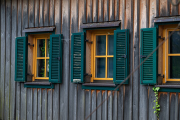 Obraz premium Close-up of weathered timber wall with yellow framed windows and green shutters, traditional Austrian alpine architecture detail.