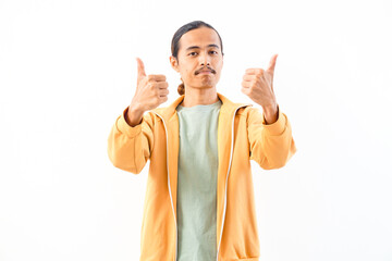 Naklejka premium Young Asian male wearing a beige jacket smiles while making a double thumbs-up gesture indoors.
