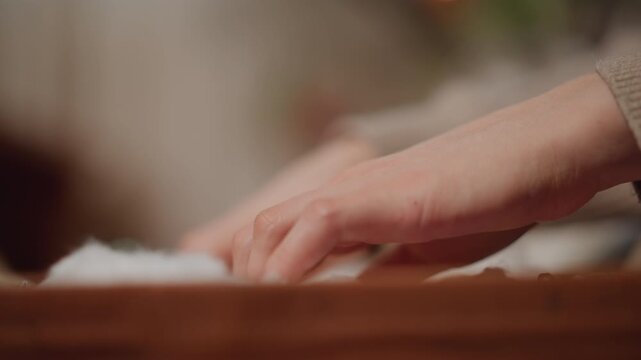 Detailed festive scene. Focus on hands arranging festive decorations with warm holiday ambiance. Intimate shot capturing hands delicately placing ornaments into wooden box amid holiday lights