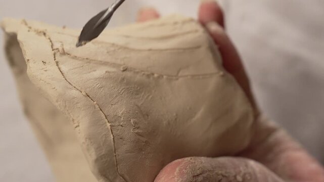 Female entrepreneur hands shaping raw mud ceramic artwork on tabletop inside studio workshop. Creative manual modeling process for small craft production startup business.