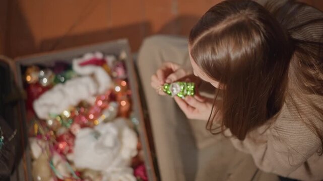 Vintage ornaments revealed by woman. Gentle woman displays aged ornaments on cozy living space floor. Woman carefully opens box to reveal cherished vintage ornaments in warm living area