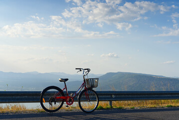 Fototapeta premium Red bicycle parked on the roadside with a beautiful scenic mountain landscape under a bright blue sky.