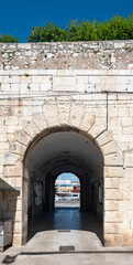 Naklejka premium Ancient Masonry Sea Gate Archway Framing A Charming European City Street Scene In Summer
