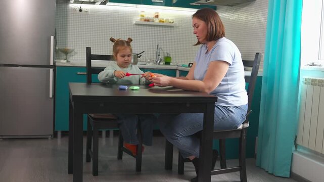 Wide show of preschool Caucasian girl is shaping clay at a table with her mother in a bright Montessori inspired space. Family activities develop imagination, problem solving