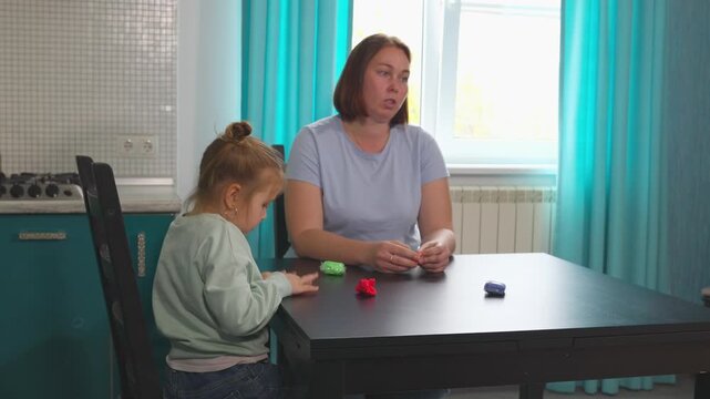 Young Caucasian child is exploring clay art at a table with her teacher in a bright home learning space. Interactive guided activities support creativity, concentration, and early education