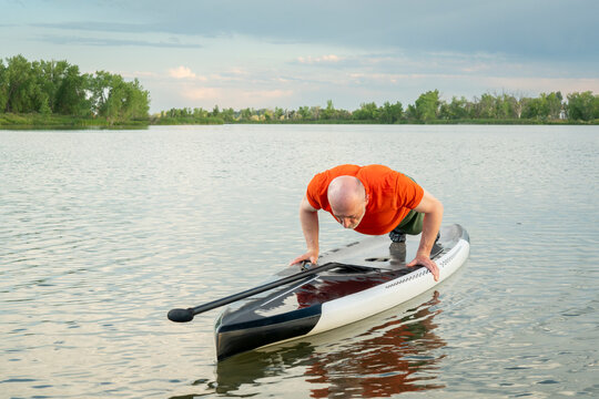 senior male doing pushups and planks for warming up on a paddleboard before paddling workout on a lake in Colorado