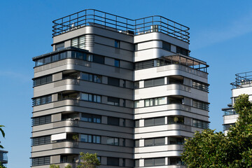 Modern residential apartment tower featuring clean geometric lines, balconies and contemporary architecture against a clear blue sky in an urban environment. © Jorge