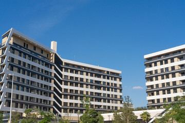 Modern apartment buildings in a contemporary residential development featuring geometric architecture, balconies and landscaped urban surroundings under a clear blue sky. © Jorge