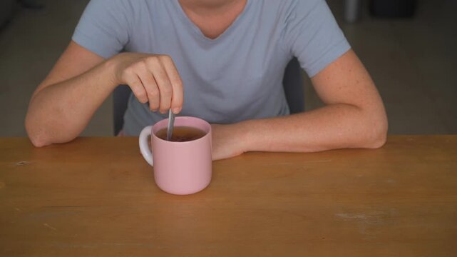 Woman stirring tea in a mug with a spoon at a table, high quality audio recording. Gentle clinking and liquid swirling sounds. Beverage preparation, relaxation and everyday lifestyle concept.
