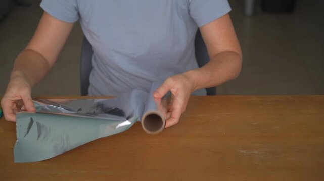 Woman unrolling aluminum foil and cutting a piece with scissors at a table, high quality audio recording. Crisp cutting and metallic rustling sounds. Kitchen task, food prep and everyday lifestyle
