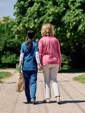 Nurse caregiver with senior woman walking outdoors and helping with shopping bag with groceries