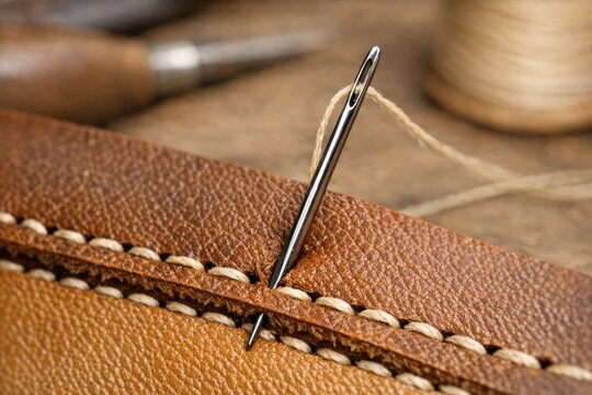 A close-up shot of a needle lying on a piece of leather, suitable for crafting or DIY projects