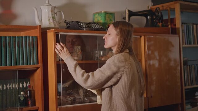 Discover old artifacts. Customer observes historic display with keen interest inside cabinet. Woman thoughtfully explores nostalgic collectible items showcased in ornate antique display case