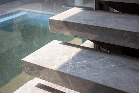 Section of minimalist grey marble steps next to a large glass window overlooking the swimming pool.