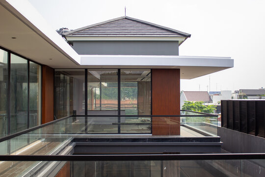 Exterior view of a luxury two-story modern residential house facade with wooden panel walls tempered glass balcony railing and gray hip roof.