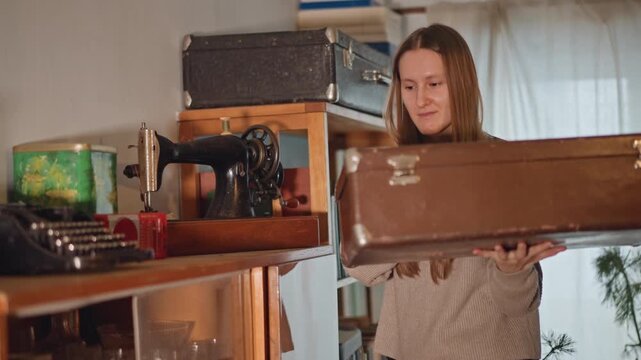 Caucasian lady reviews family keepsake. Female individual inspects vintage family memorabilia. Caucasian woman gently lifts suitcase lid to explore historical textiles and sewing artifacts
