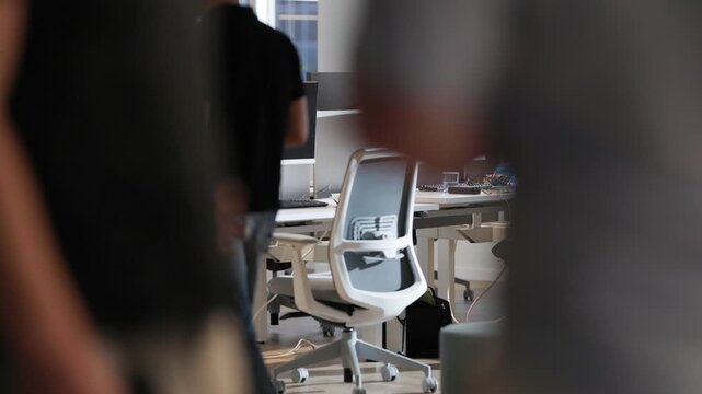 Group of individuals walking through a modern office space with ergonomic chairs and computer desks, showcasing a collaborative work environment in a bright setting