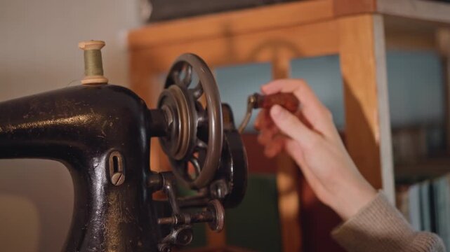 Closeup vintage sewing machine hand threading needle and adjusting wheel, seamstress restoring Singerstyle machine in cozy workshop warm lamp light highlights metal patina, spool and bobbin, careful